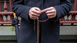 A Pell supporter prays while holding rosary beads outside court. Picture: AFP